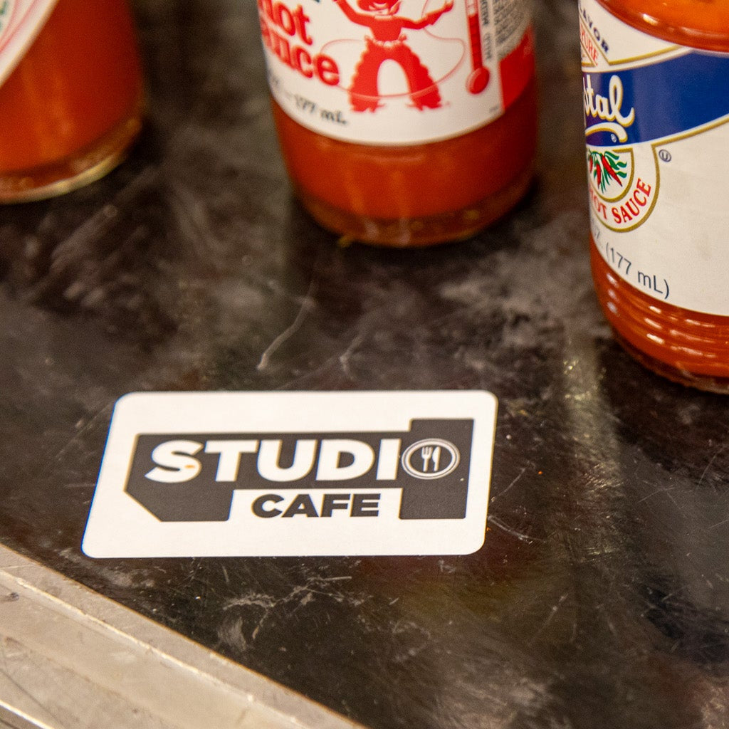 Bottles of hot sauce on a black countertop with a 'Studi Cafe' sticker.