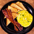 Plate with scrambled eggs, two pieces of bacon, and four slices of toast.