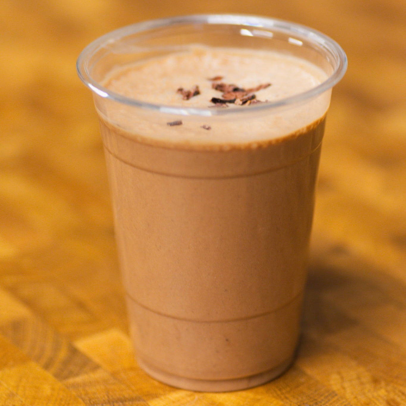 Plastic cup with a chocolate banana smoothie on a wooden surface.