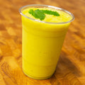 Mango mint smoothie in a clear plastic cup with mint leaves on a wooden table