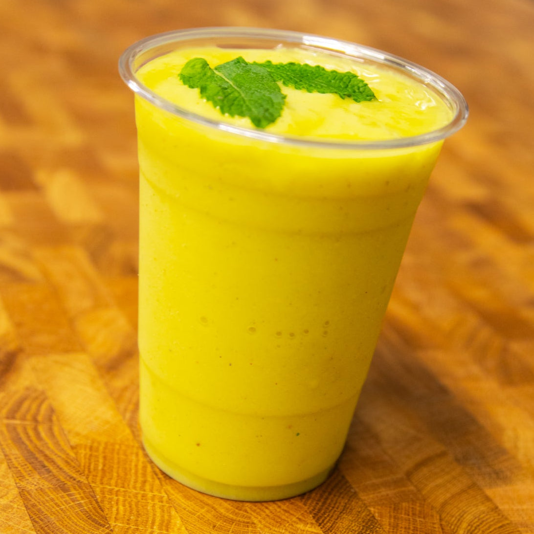 Mango mint smoothie in a clear plastic cup with mint leaves on a wooden table