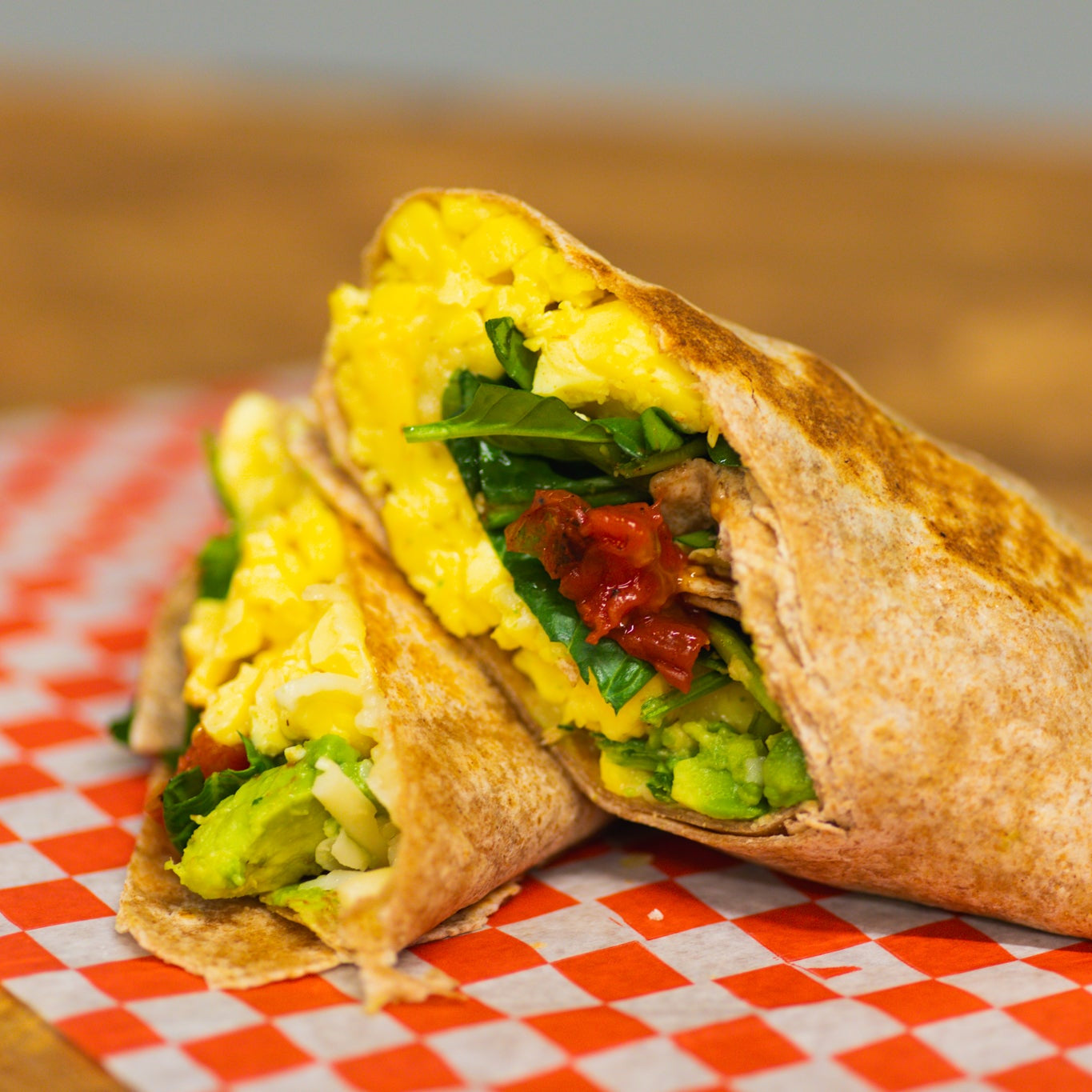 Breakfast wrap with eggs, spinach, and other fillings on a checkered paper.
