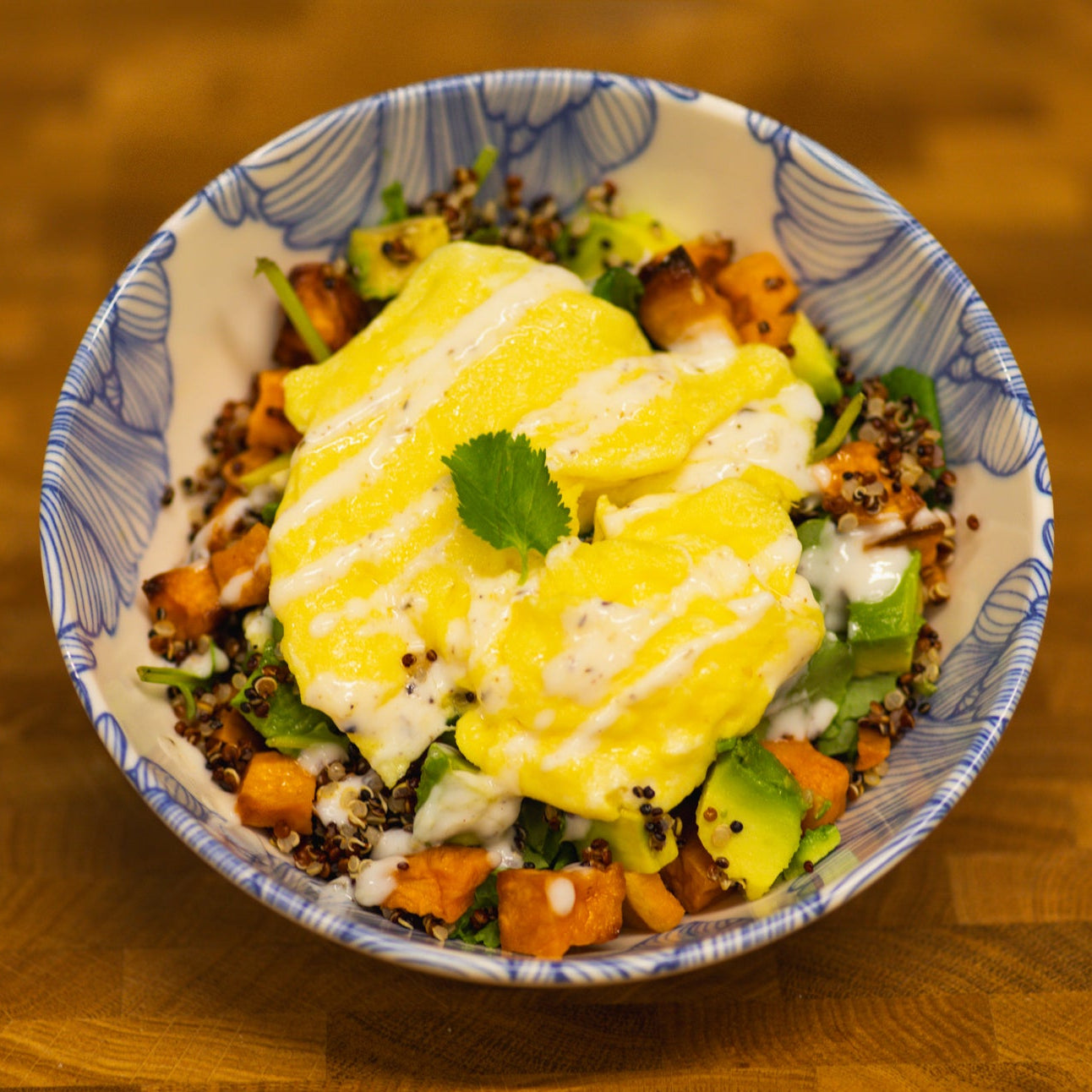 Breakfast protein bowl with scrambled egg, quinoa, sweet potato, kale, avocado, and lemon yogurt sauce.