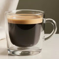 Clear glass mug with an Americano beverage on a neutral background