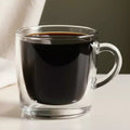 Clear glass mug with black coffee on a neutral background