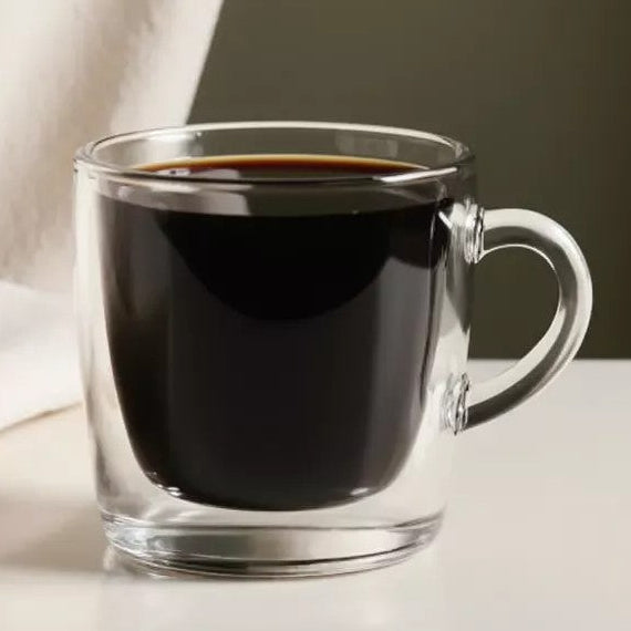 Clear glass mug with black coffee on a neutral background