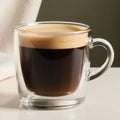 Clear glass mug with a shot of espresso with a neutral background