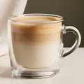 Clear glass mug with latte drink on a neutral background