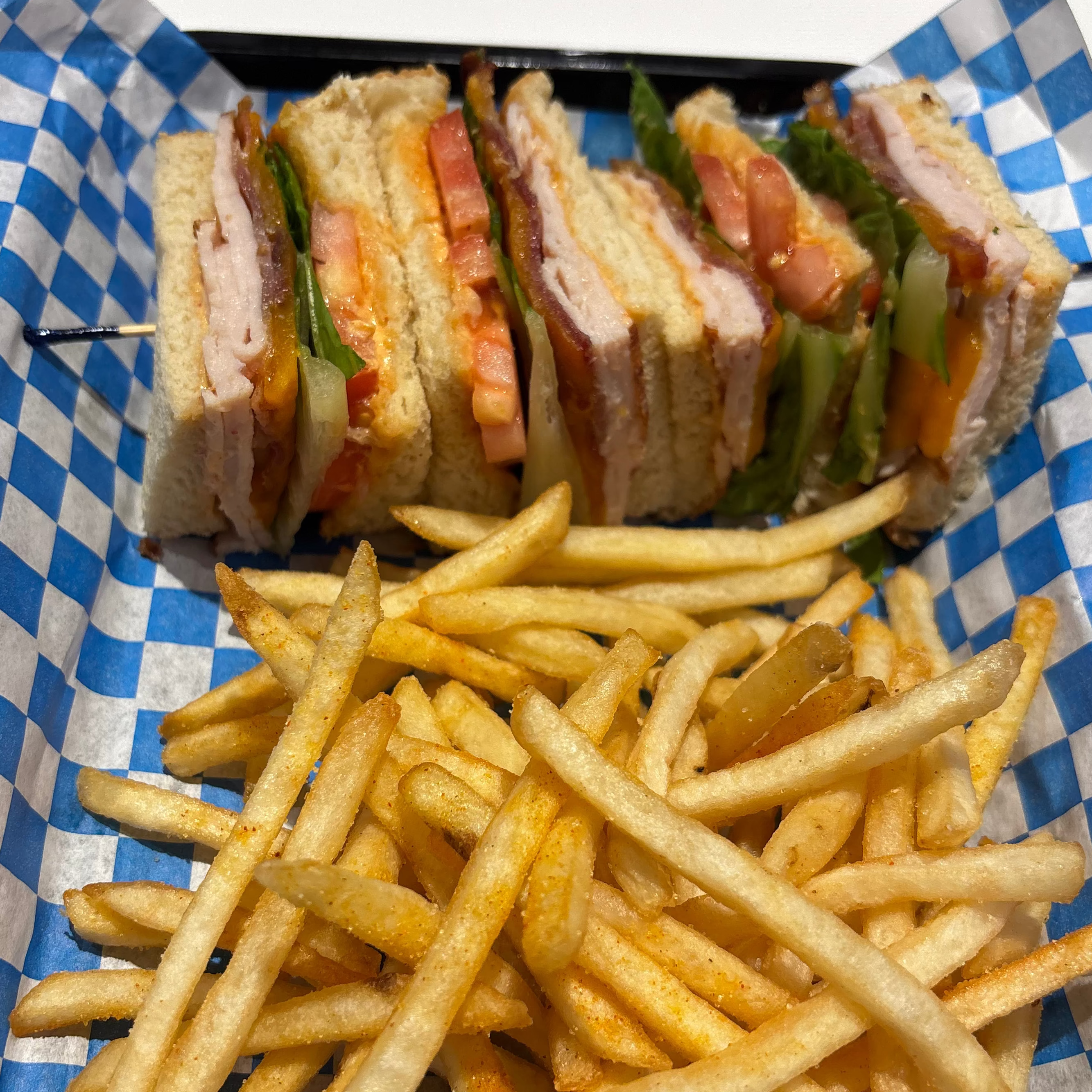 Club sandwich and French fries on a blue and white checkered paper